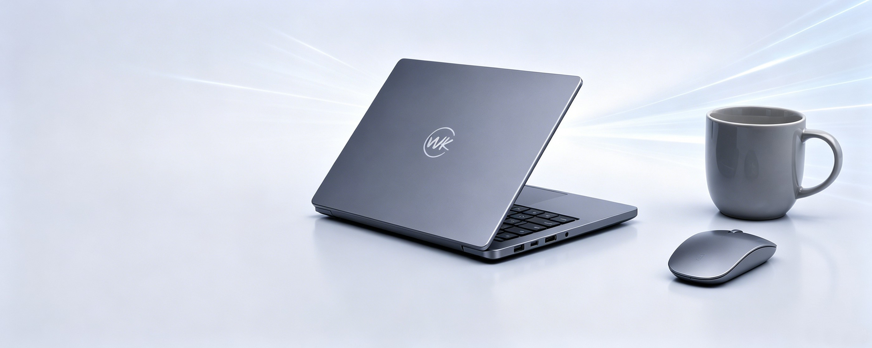 WK Core i3 laptop in dark gray with WK logo on lid, styled with a gray ceramic mug and wireless mouse on a soft blue desk